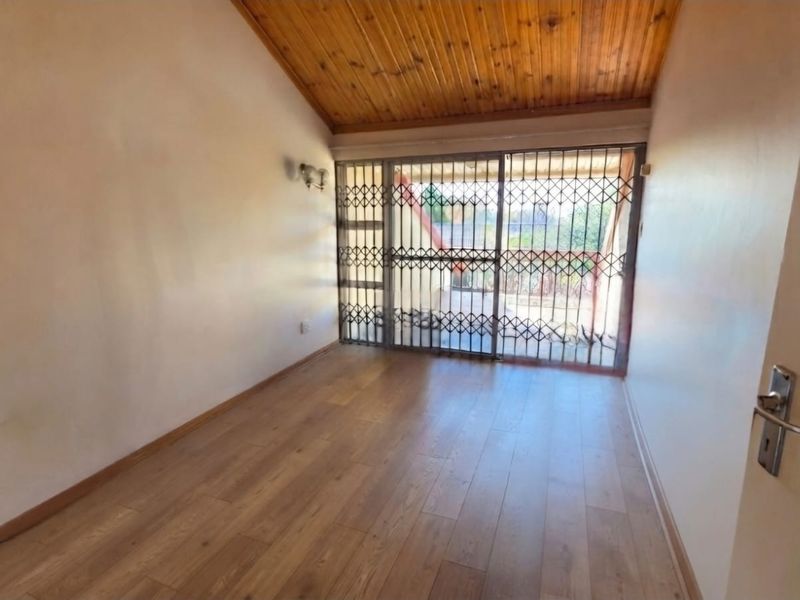 An empty bedroom featuring laminate flooring, a vaulted timber ceiling, and a sliding door with a security gate leading to the exterior.