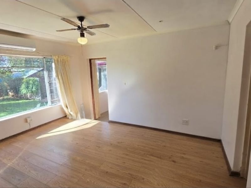 A bright, empty bedroom featuring laminate flooring, a ceiling fan, and a wall-mounted split-system air conditioner with views of the garden.