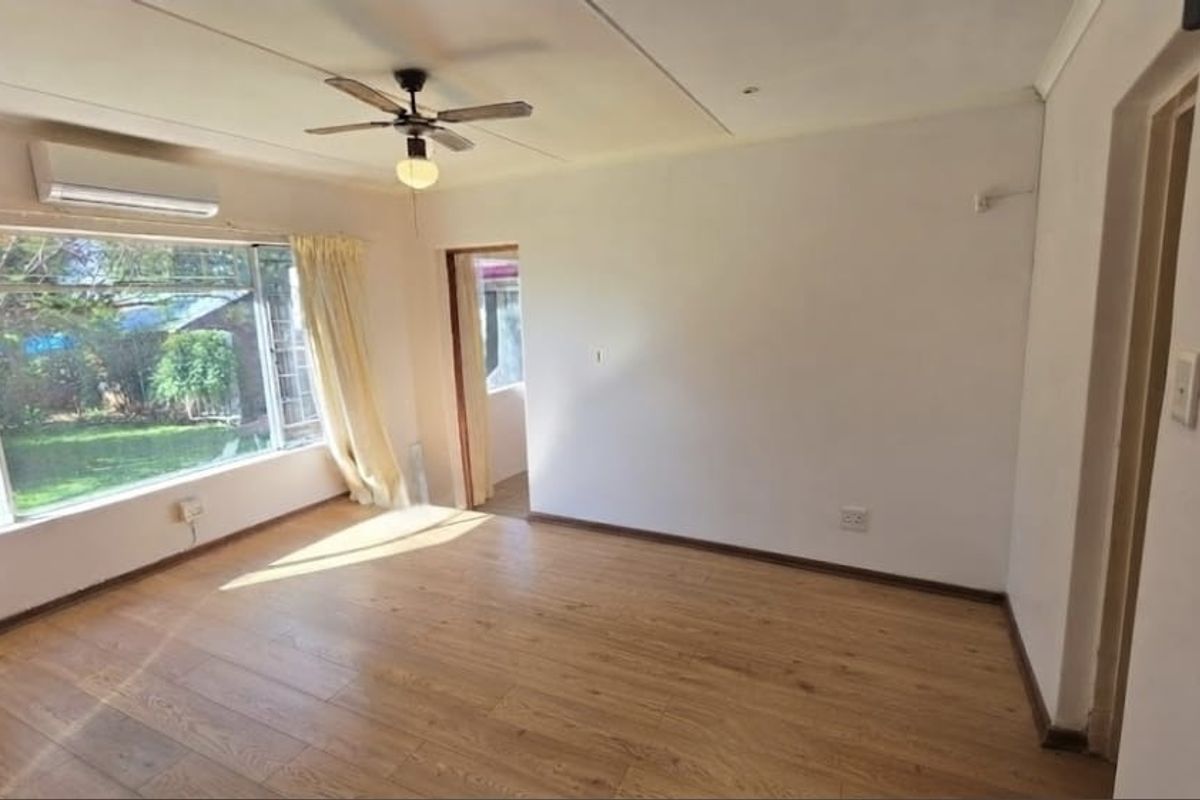 A bright, empty bedroom featuring laminate flooring, a ceiling fan, and a wall-mounted split-system air conditioner with views of the garden.
