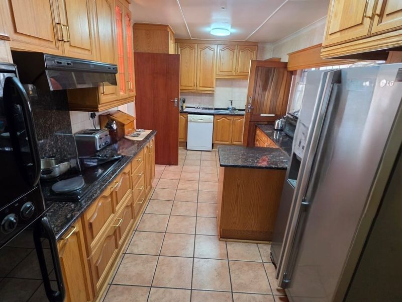 A functional kitchen featuring traditional wooden cabinetry, granite countertops, tiled flooring, and integrated appliances including an oven and extractor fan.