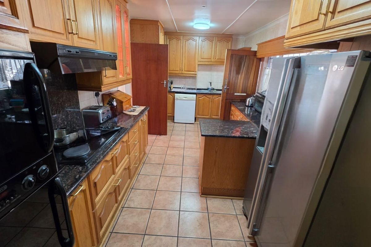 A functional kitchen featuring traditional wooden cabinetry, granite countertops, tiled flooring, and integrated appliances including an oven and extractor fan.