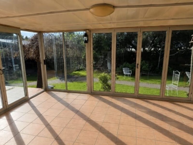 A bright, enclosed patio featuring tiled flooring and extensive glass sliding doors that provide a seamless connection to the garden.