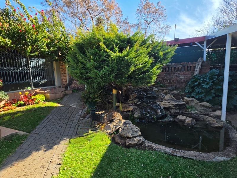 A landscaped rear garden featuring a stone water feature, a small pond, and a brick paved pathway leading to a covered patio area.