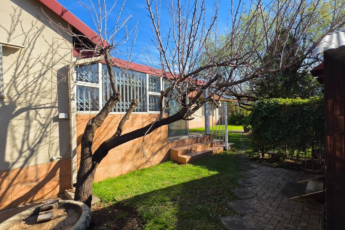 Rear exterior view of the house featuring a tiled facade, security gates, paved walkway, and a small garden area.