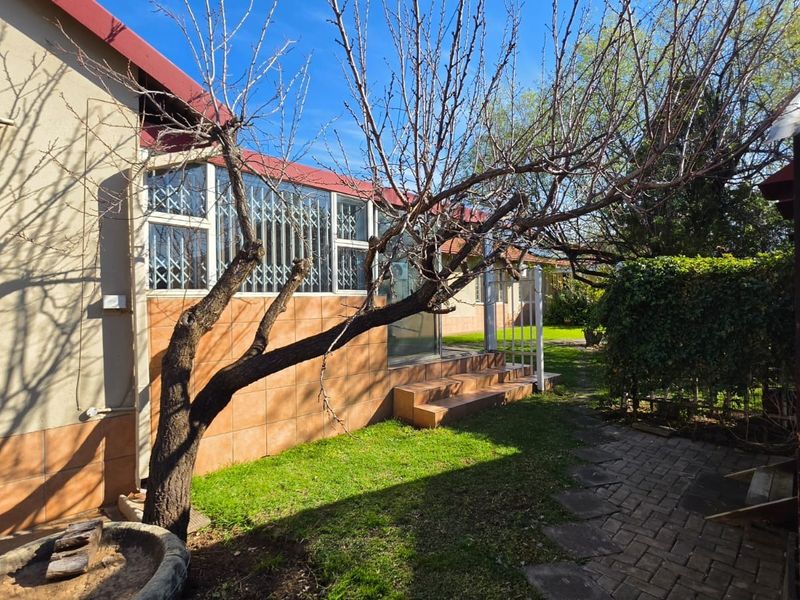 Rear exterior view of the house featuring a tiled facade, security gates, paved walkway, and a small garden area.