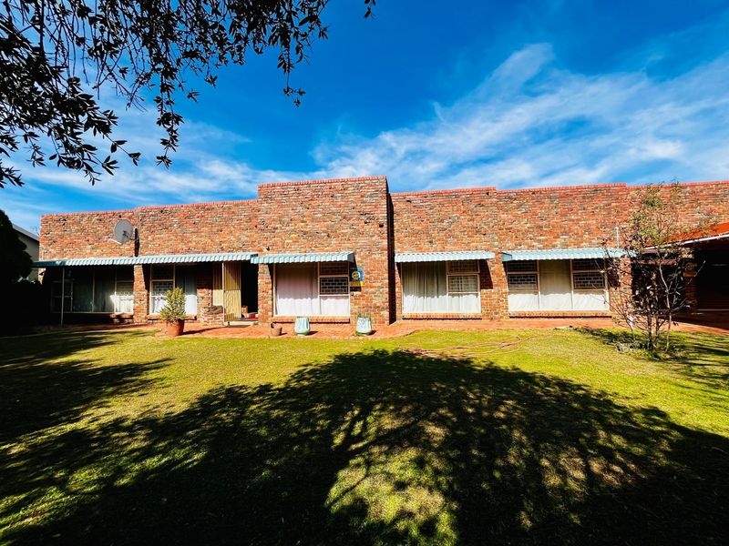 Rear view of a face brick house featuring a paved patio area and a spacious lawn under a clear blue sky.