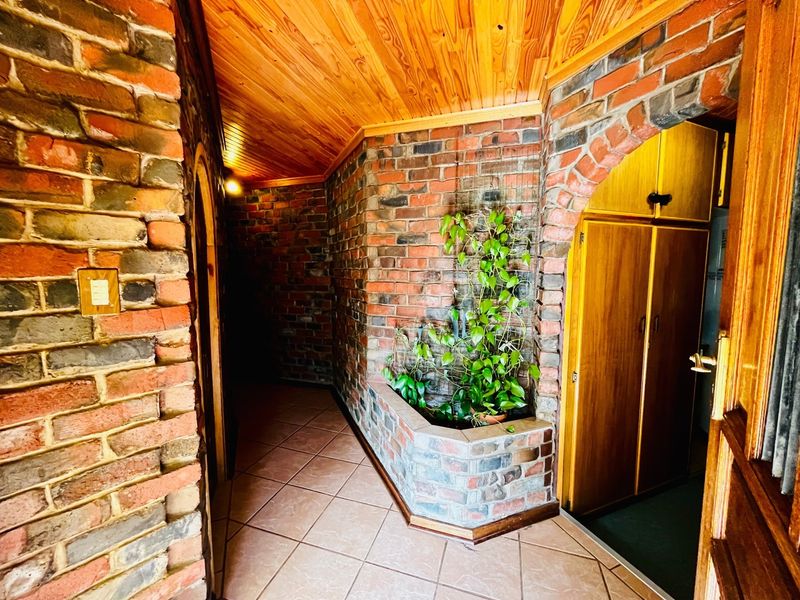 A rustic hallway featuring exposed brick walls, a warm timber ceiling, tiled flooring, and a unique built-in brick planter.