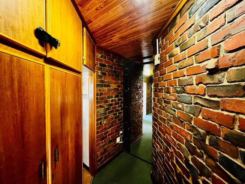 A narrow hallway featuring exposed brick walls, a timber-paneled ceiling, and extensive built-in wooden cabinetry, offering a rustic aesthetic with potential for modernization.