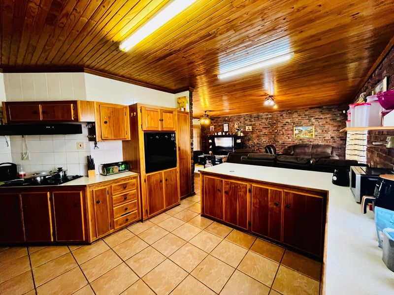 Open-plan kitchen and living area featuring a timber-clad ceiling, exposed brick wall, tiled flooring, and traditional wooden cabinetry with built-in appliances.