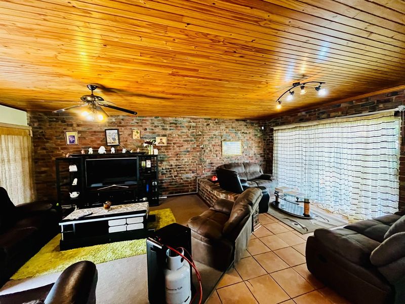 Spacious living room featuring exposed brick walls, a warm timber ceiling, tiled flooring, and a built-in brick fireplace hearth.