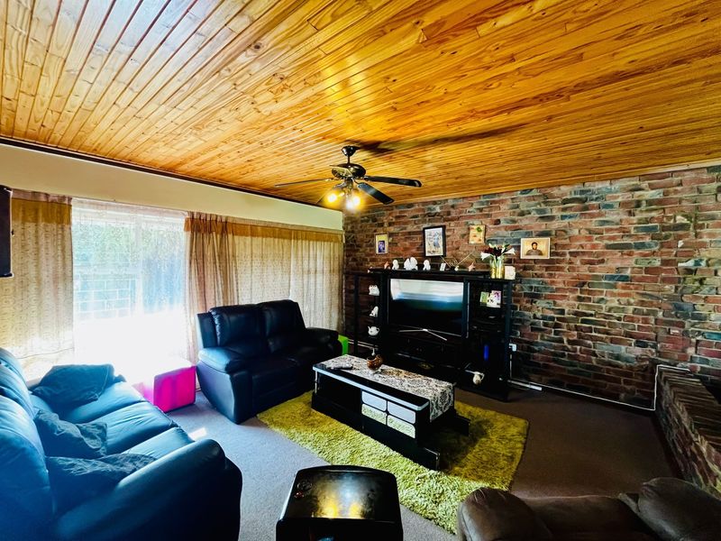 A living room featuring a distinctive exposed brick wall and a warm timber tongue and groove ceiling with an integrated ceiling fan.