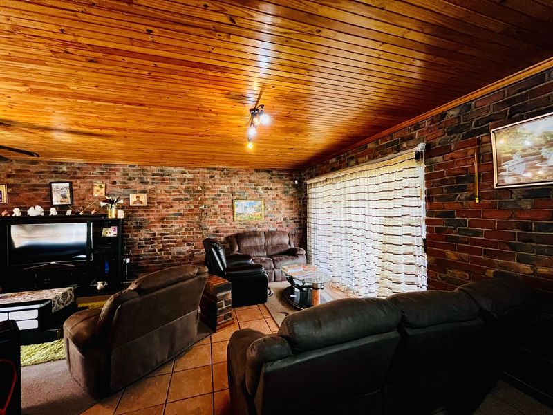 A living room featuring exposed brick walls, a warm timber-paneled ceiling, and ceramic floor tiles, with direct access to the outdoors via a sliding door.