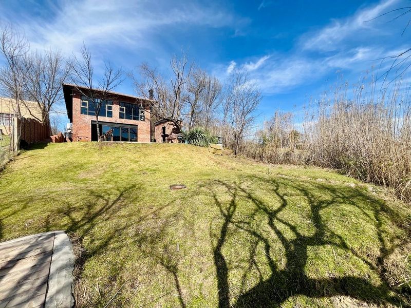 Rear view of a two-story exposed brick house featuring large glass sliding doors and a spacious sloping lawn area.