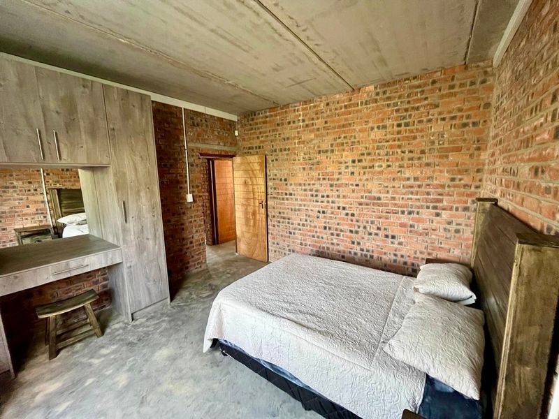 Industrial-style bedroom featuring exposed brick walls, polished concrete flooring, an exposed concrete ceiling, and integrated built-in cabinetry with a vanity.