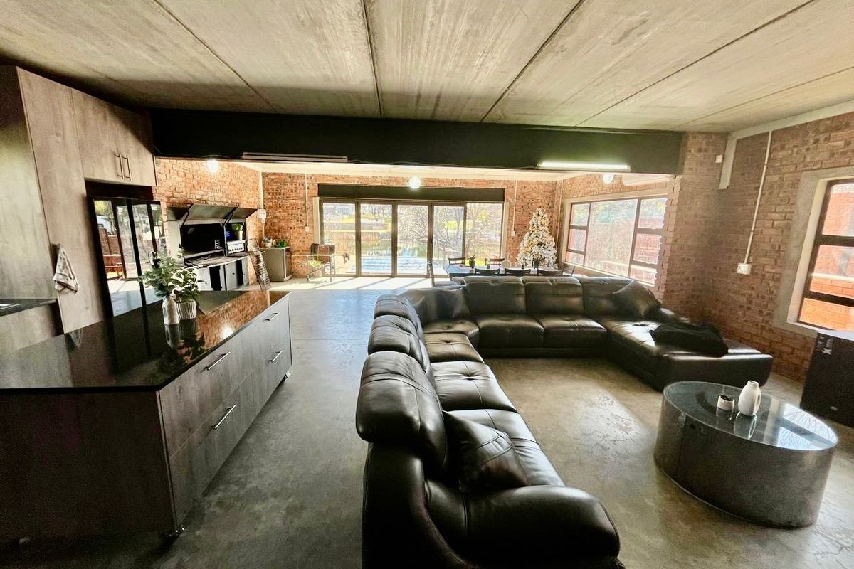 Spacious open-plan living area featuring industrial-style exposed brick walls, concrete ceilings, polished concrete floors, and a modern kitchen island with direct patio access.