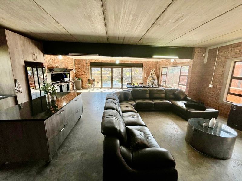 Spacious open-plan living area featuring industrial-style exposed brick walls, concrete ceilings, polished concrete floors, and a modern kitchen island with direct patio access.
