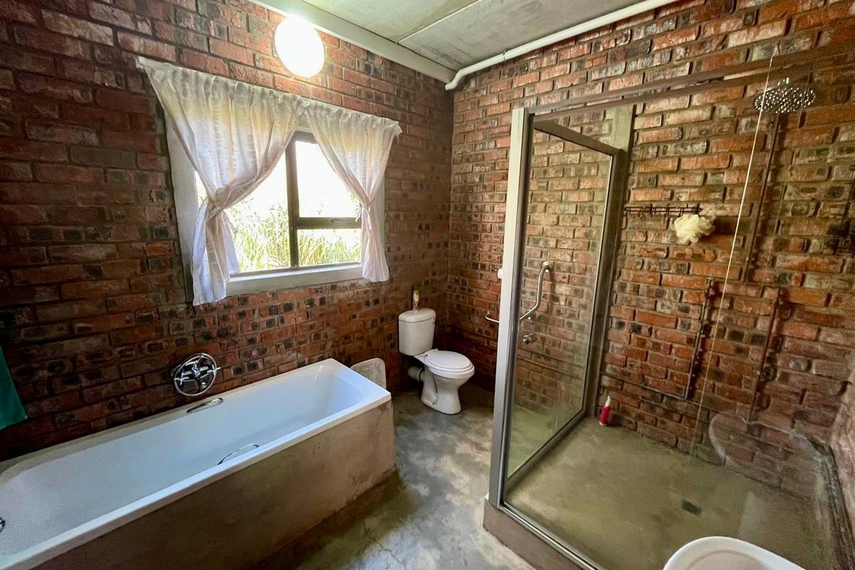 Bathroom featuring exposed brick walls, a built-in bathtub, a glass-enclosed shower with a rain shower head, and concrete flooring.