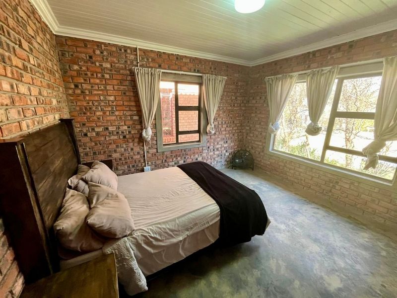 A bedroom featuring exposed brick walls, polished concrete flooring, and large windows allowing for natural light.