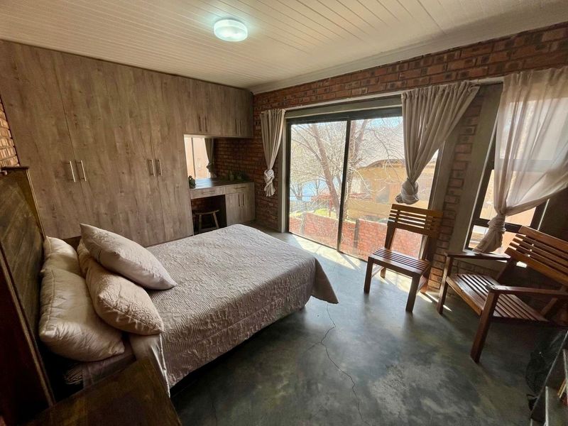 Bedroom featuring exposed brick walls, concrete flooring, built-in cupboards with a vanity area, and a sliding glass door providing natural light.