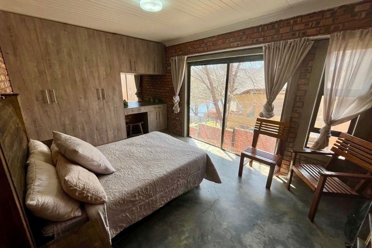 Bedroom featuring exposed brick walls, concrete flooring, built-in cupboards with a vanity area, and a sliding glass door providing natural light.