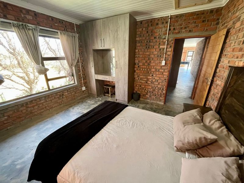 Bedroom featuring exposed brick walls, concrete flooring, timber ceiling, and a built-in wardrobe with an integrated vanity unit.