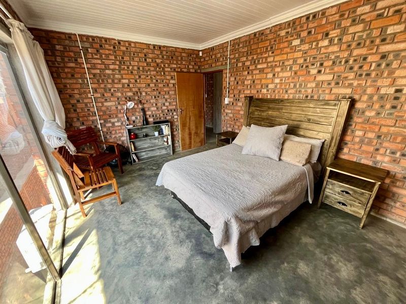 A rustic bedroom featuring exposed brick walls, polished concrete flooring, and a sliding glass door providing natural light.