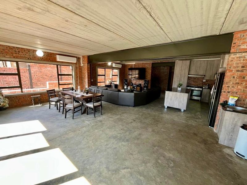 Spacious open-plan living area featuring industrial-style exposed brick walls, concrete ceilings, polished concrete floors, and a modern integrated kitchen.