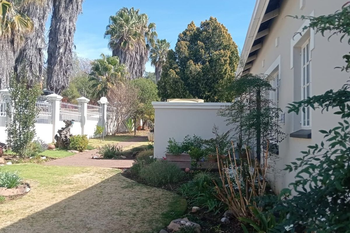 A well-maintained rear garden area featuring a paved walkway, established landscaping, and secure perimeter walling with fencing.