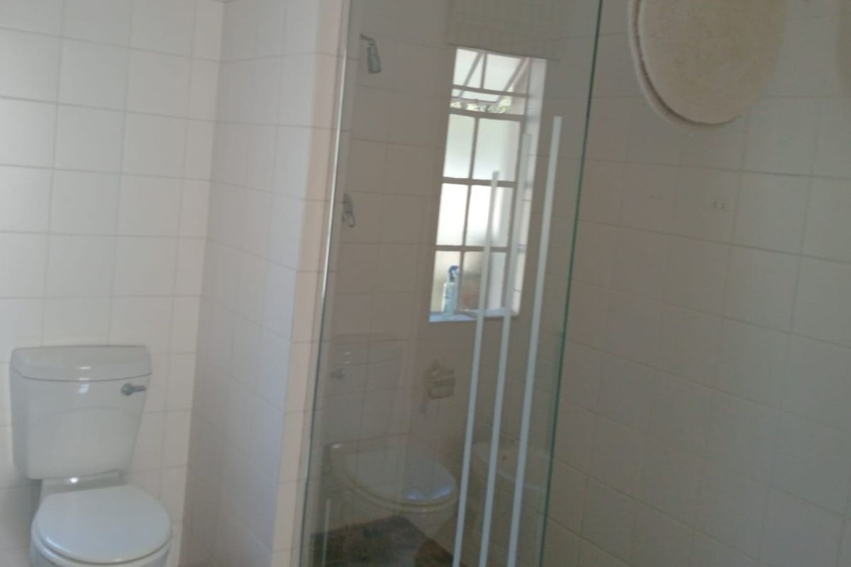 A functional bathroom featuring white wall tiles, a standard toilet, and a glass-enclosed shower area with a window for natural light.