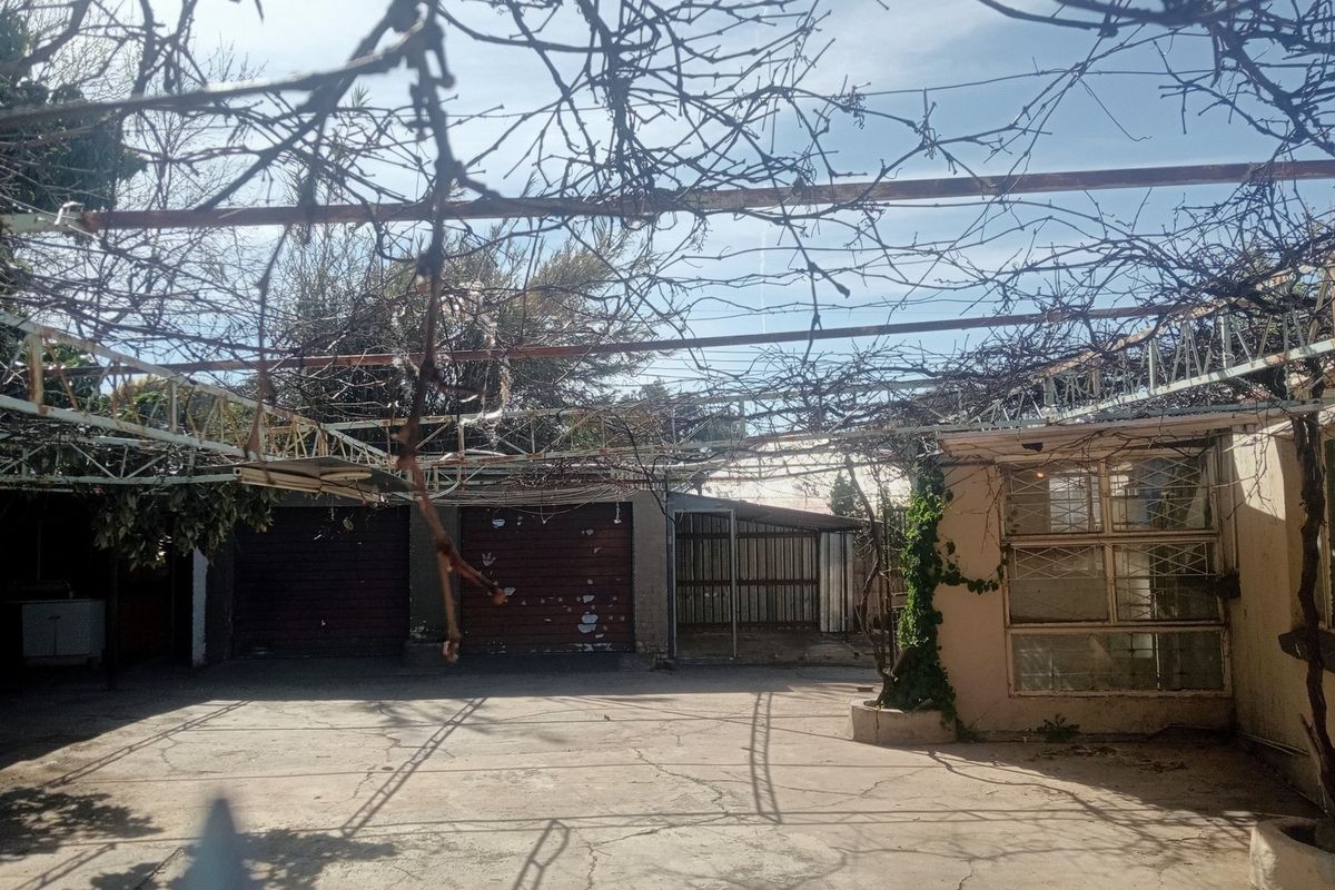 Rear exterior area featuring a large concrete paved space, a weathered metal pergola structure, and access to garage facilities.