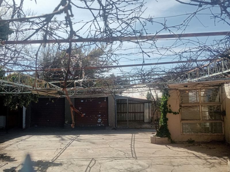 Rear exterior area featuring a large concrete paved space, a weathered metal pergola structure, and access to garage facilities.