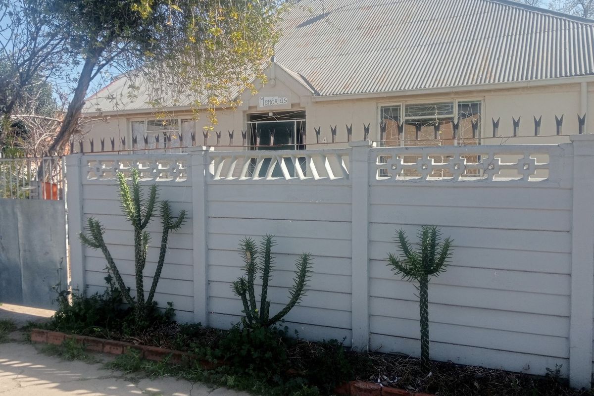 Front view of a residential property featuring a precast concrete boundary wall with security spikes and a corrugated metal roof.
