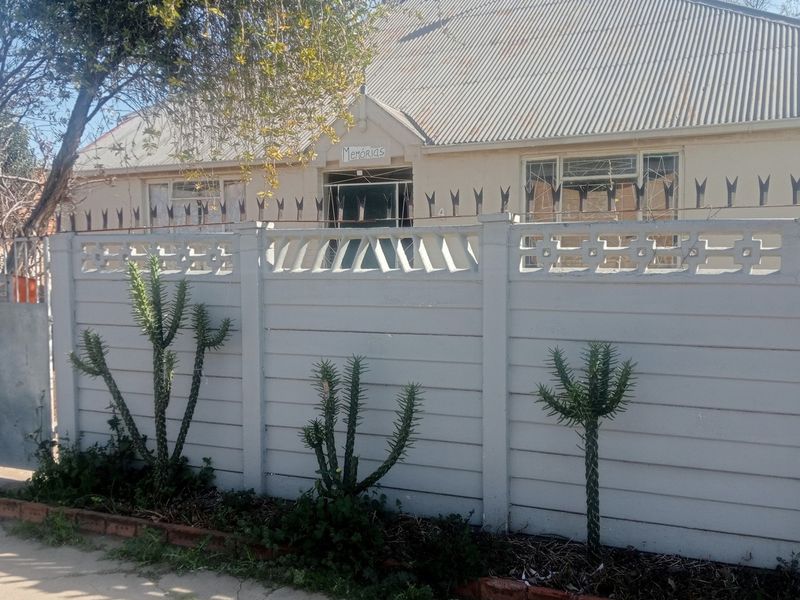 Front view of a residential property featuring a precast concrete boundary wall with security spikes and a corrugated metal roof.