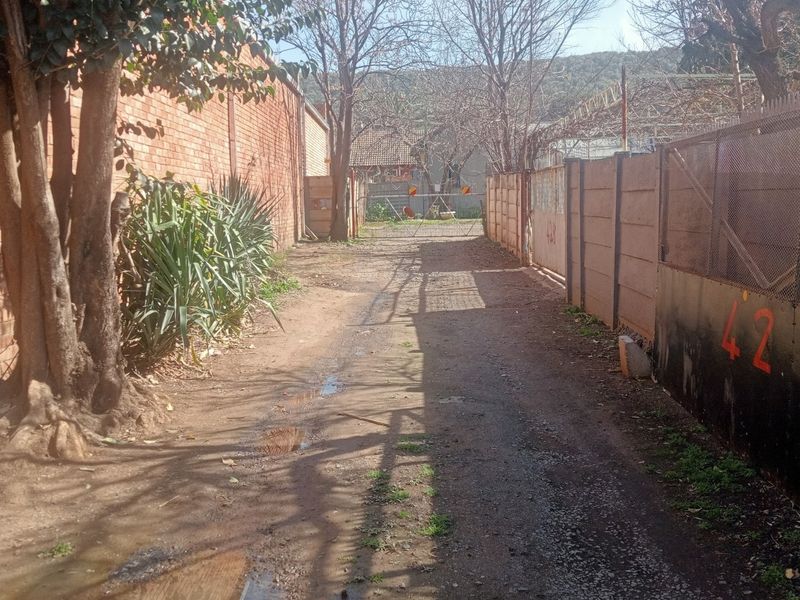 A narrow rear access path or alleyway featuring brick and precast concrete boundary walls with metal security fencing.