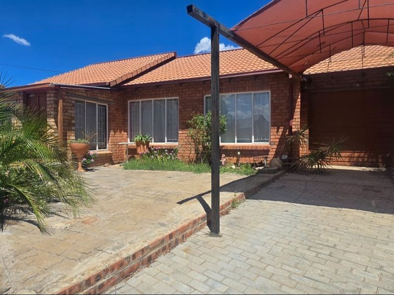 Front exterior view of a face brick townhouse featuring a tiled roof, paved driveway, and a covered carport area.