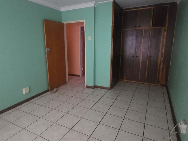 An empty bedroom featuring tiled flooring and built-in wooden cupboards, offering a blank canvas for renovation or restyling.
