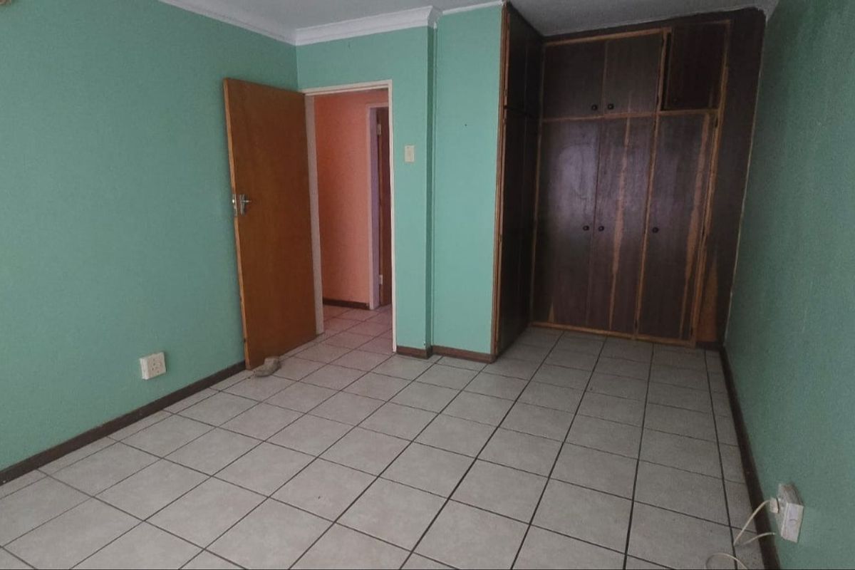 An empty bedroom featuring tiled flooring and built-in wooden cupboards, offering a blank canvas for renovation or restyling.