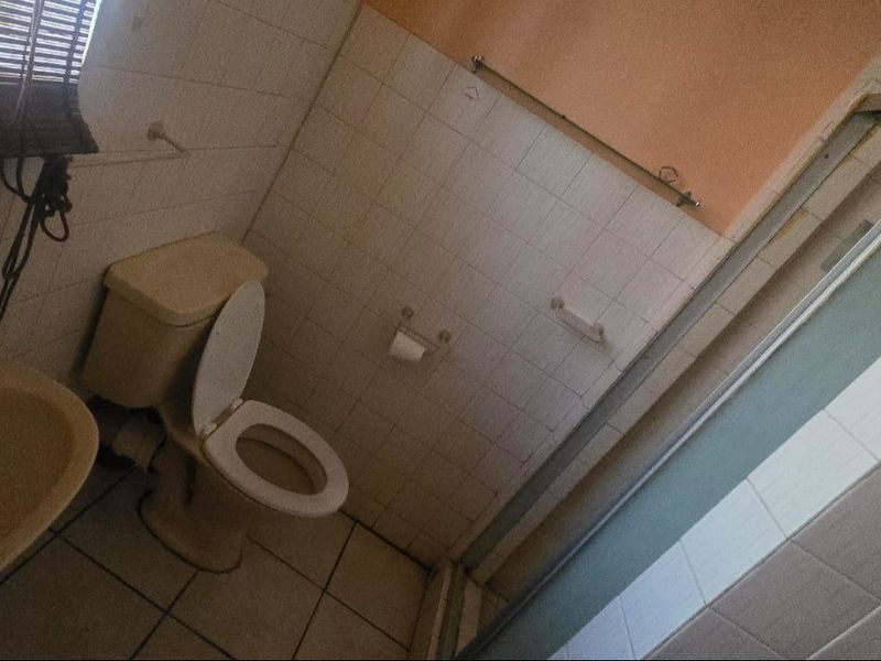A dated bathroom featuring a standard toilet, washbasin, and shower enclosure with tiled finishes, requiring modernization to improve aesthetic appeal.