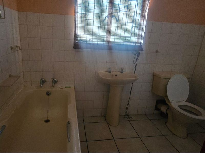 A dated bathroom featuring a pedestal basin, bathtub, and toilet with original ceramic tiling, offering potential for a modern renovation.