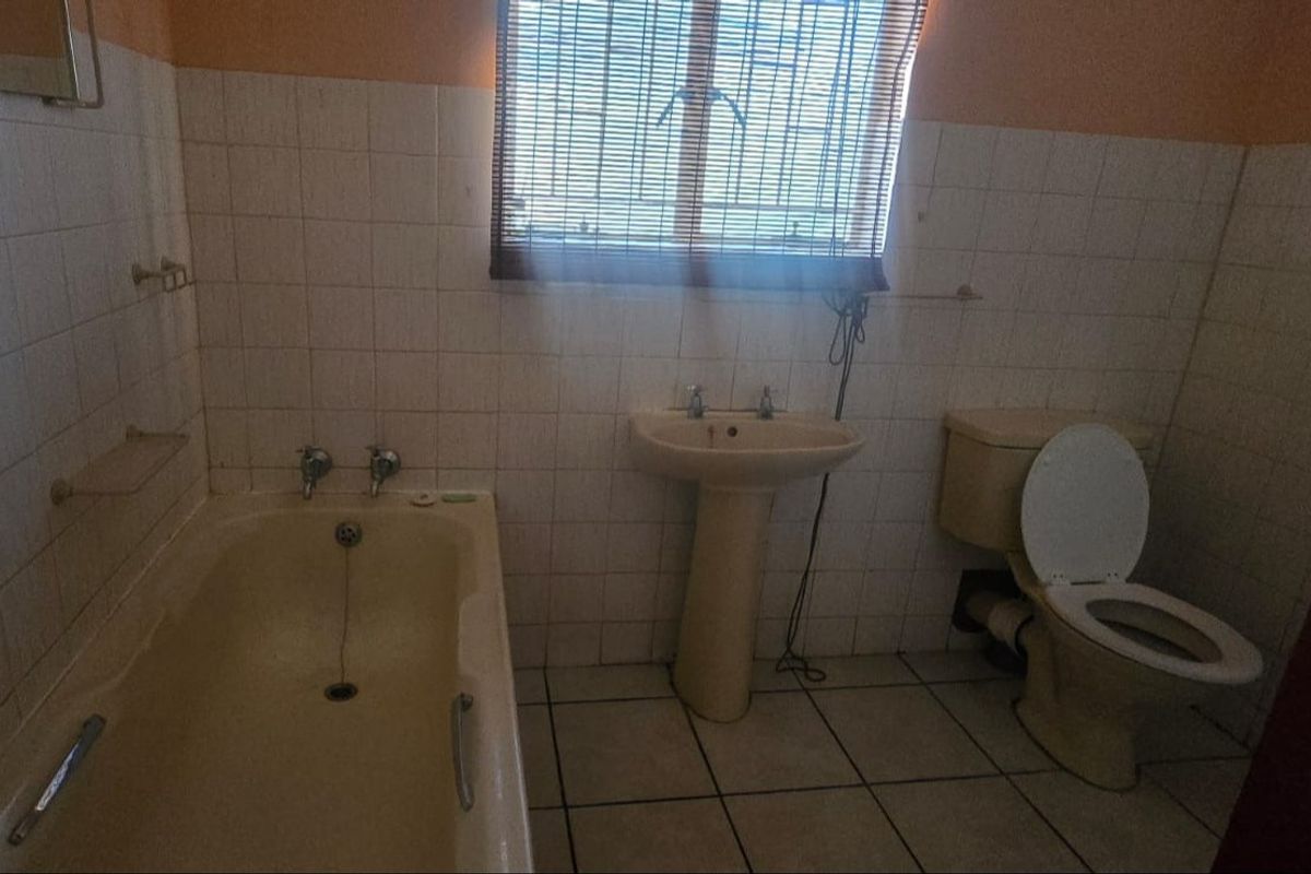 A dated bathroom featuring a pedestal basin, bathtub, and toilet with original ceramic tiling, offering potential for a modern renovation.