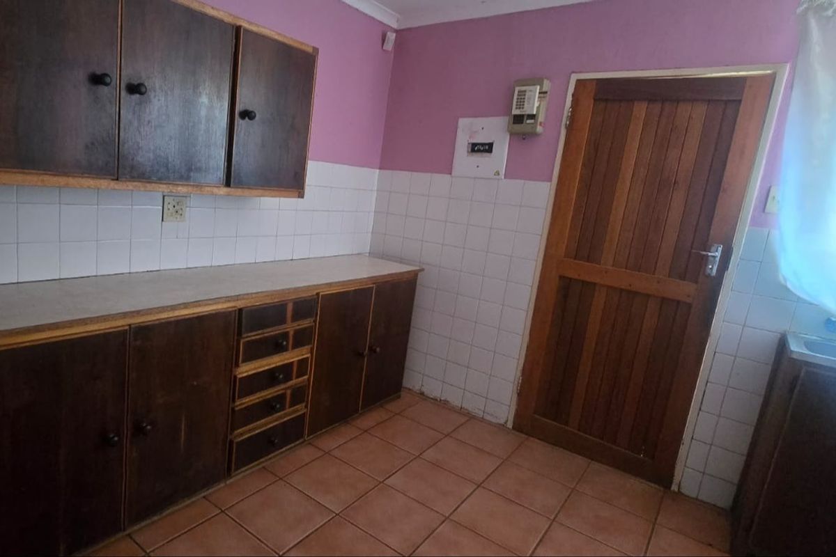 A dated kitchen featuring dark wooden cabinetry, tiled splashbacks, and tiled flooring, with a wooden door leading to the exterior.