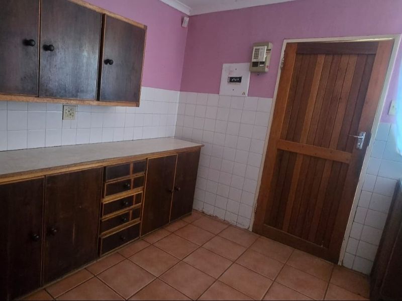 A dated kitchen featuring dark wooden cabinetry, tiled splashbacks, and tiled flooring, with a wooden door leading to the exterior.