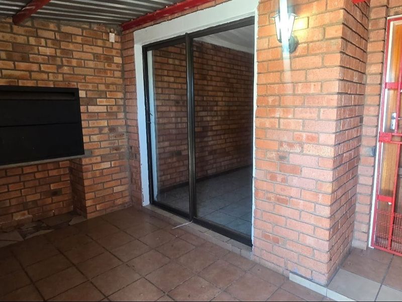 Covered patio area featuring exposed brick walls, a built-in braai, tiled flooring, and a secure sliding door entrance.