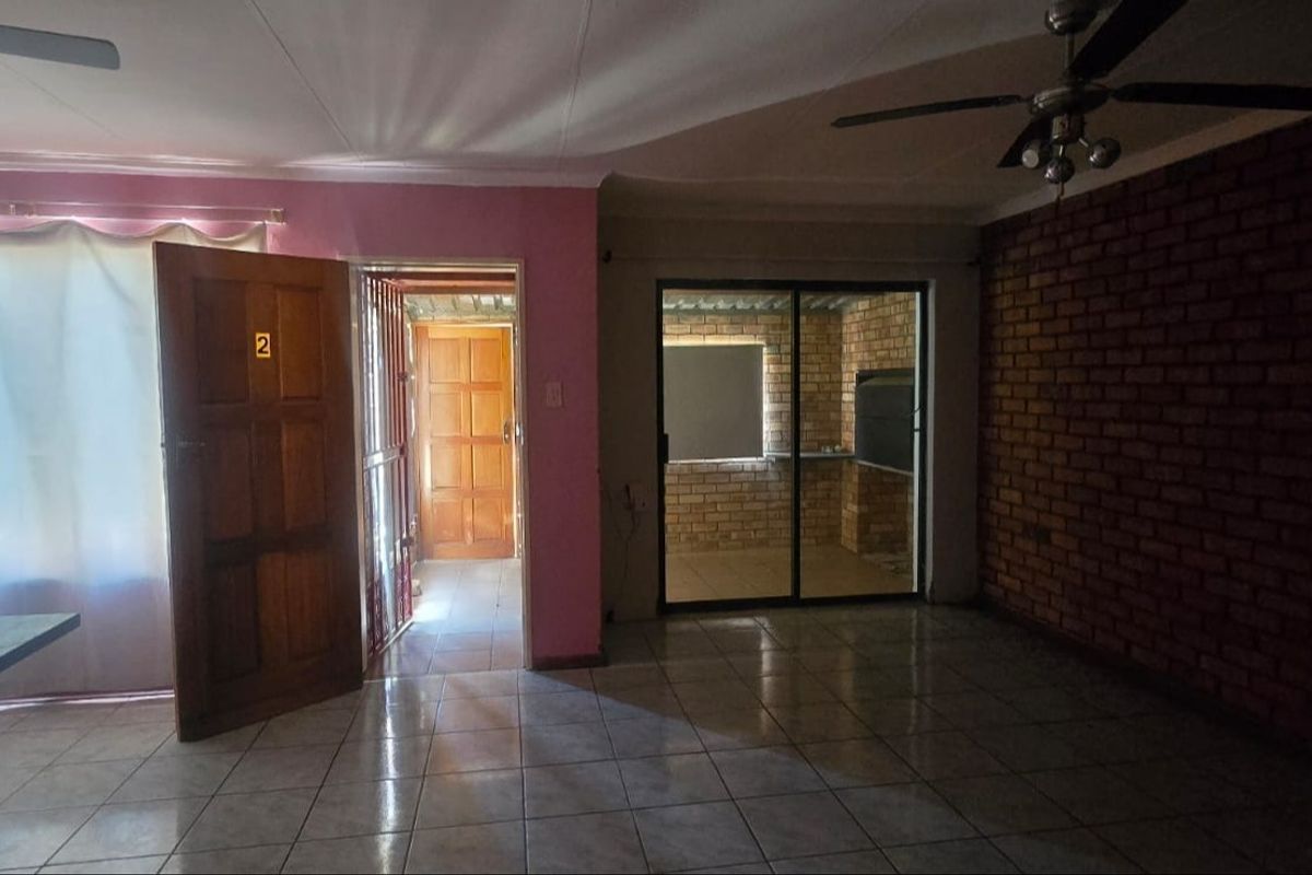 Spacious living area featuring tiled flooring, an exposed brick feature wall, and a sliding glass door leading to an enclosed patio area.