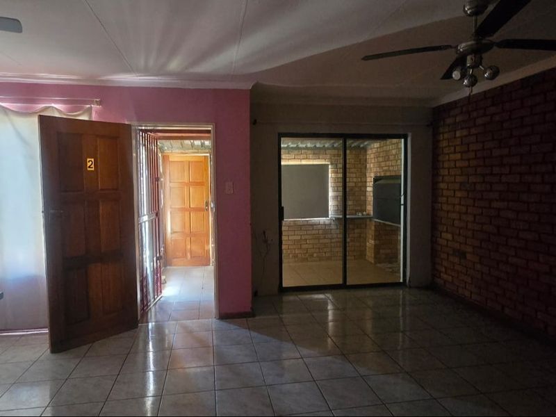 Spacious living area featuring tiled flooring, an exposed brick feature wall, and a sliding glass door leading to an enclosed patio area.