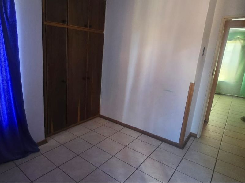 An empty bedroom featuring tiled flooring and built-in wooden cupboards, offering a blank canvas for renovation or restyling.