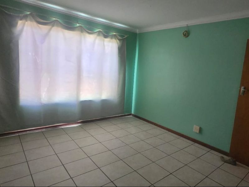 An empty bedroom featuring tiled flooring, green painted walls, and a timber door, offering a blank canvas for potential renovation or restyling.
