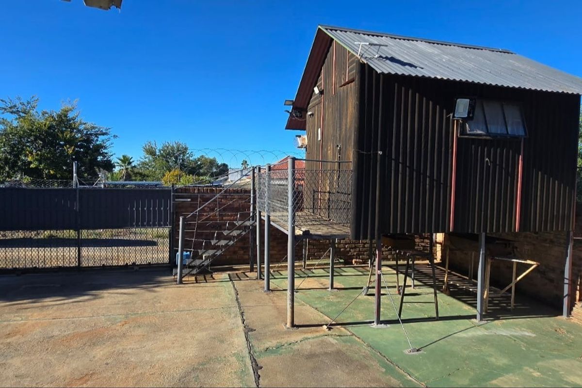 Rear exterior view of a townhouse property featuring a raised metal structure, concrete paving, and secure boundary fencing with razor wire.