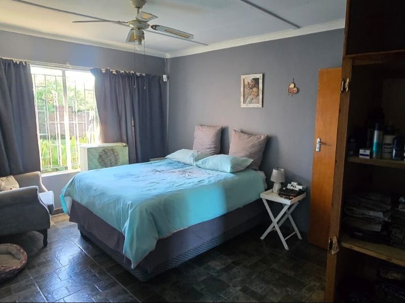 A functional bedroom featuring tiled flooring, a ceiling fan, and window security bars, offering a comfortable and practical living space.