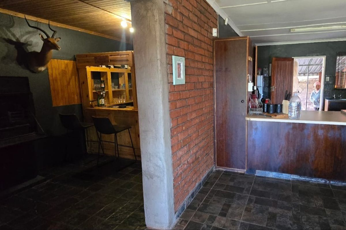 Open plan living area featuring a built-in bar, exposed brick wall, and kitchen space with dark cabinetry and tiled flooring.